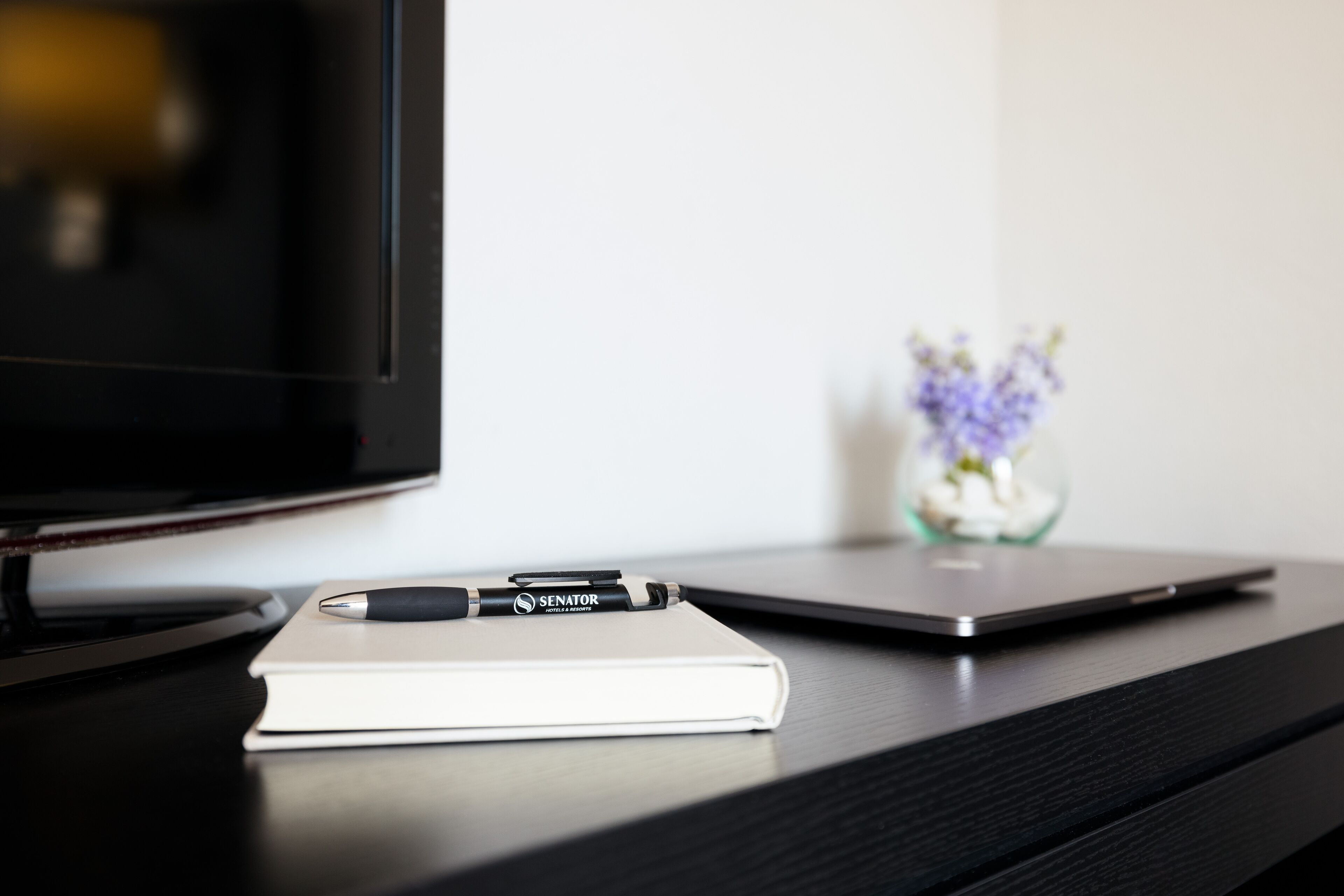 A desk with a laptop, a notebook, and a pen.