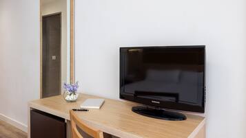 A hotel room with a wooden desk, a Samsung TV, a mirror, a vase with flowers, and a notebook.