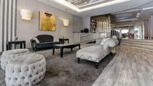 A modern living room with tufted ottomans, a black sofa, and a grey sofa. There is a staircase leading to an upper level.