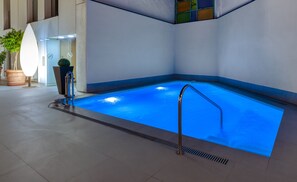 An indoor swimming pool with clear blue water, a metal ladder, and a tiled floor. - Virgen de los Reyes Hotel (Seville)