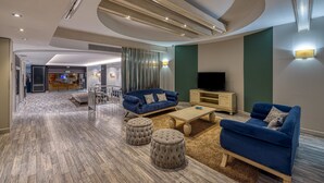 Un salon moderne avec un canapé bleu, des poufs, une table basse et un téléviseur.