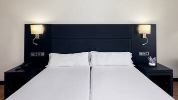Ein Doppelbett mit weißen Bettwäsche, zwei Nachttische mit Lampen und ein kleiner Blumenstrauß auf dem rechten Tisch.