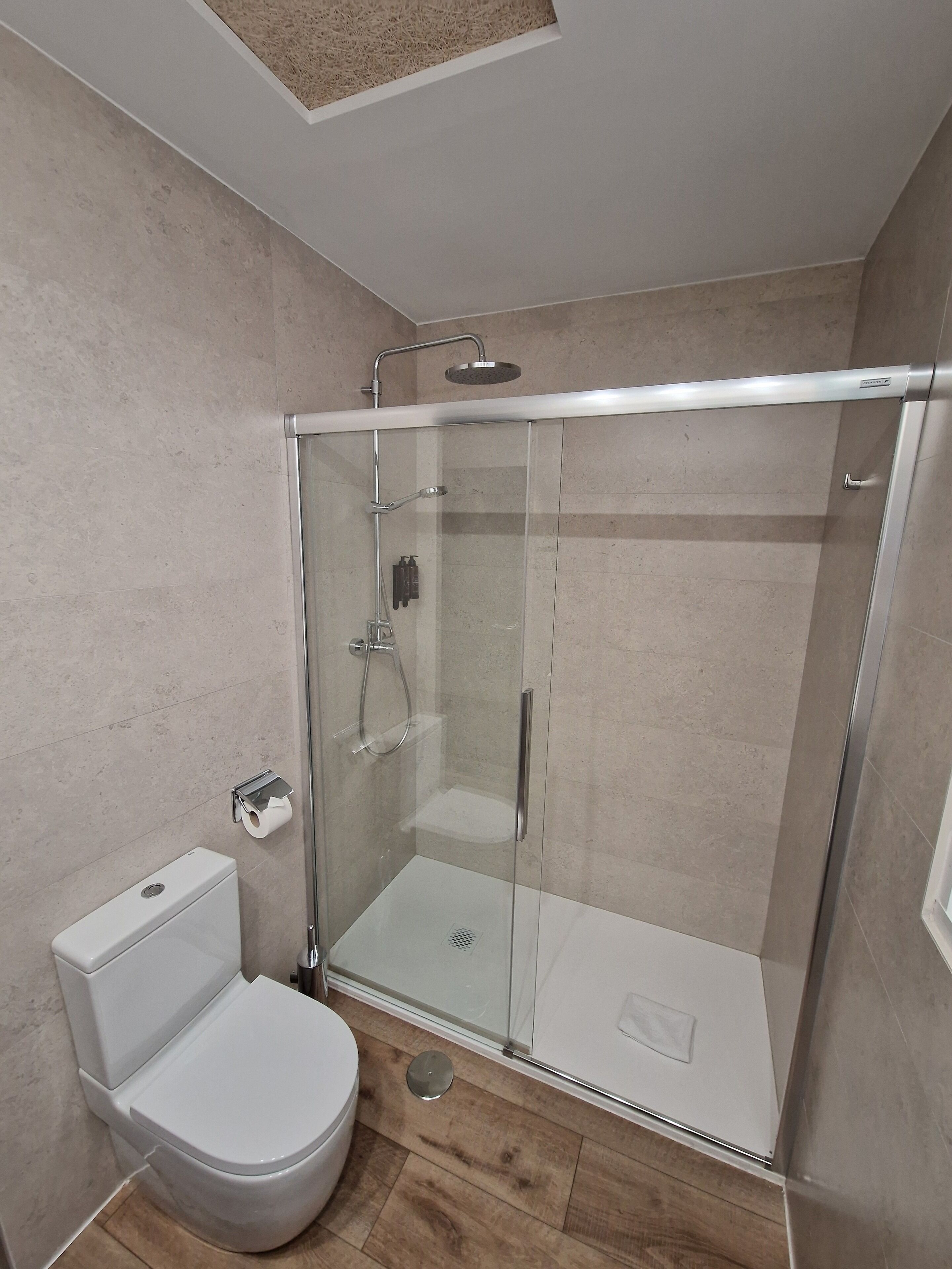 Un bagno moderno con doccia vetrata, water bianco e pavimento piastrellato.