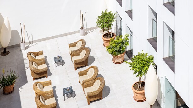 Une terrasse sur le toit, aménagée avec des meubles en osier, des plantes en pot et un bâtiment moderne en arrière-plan.