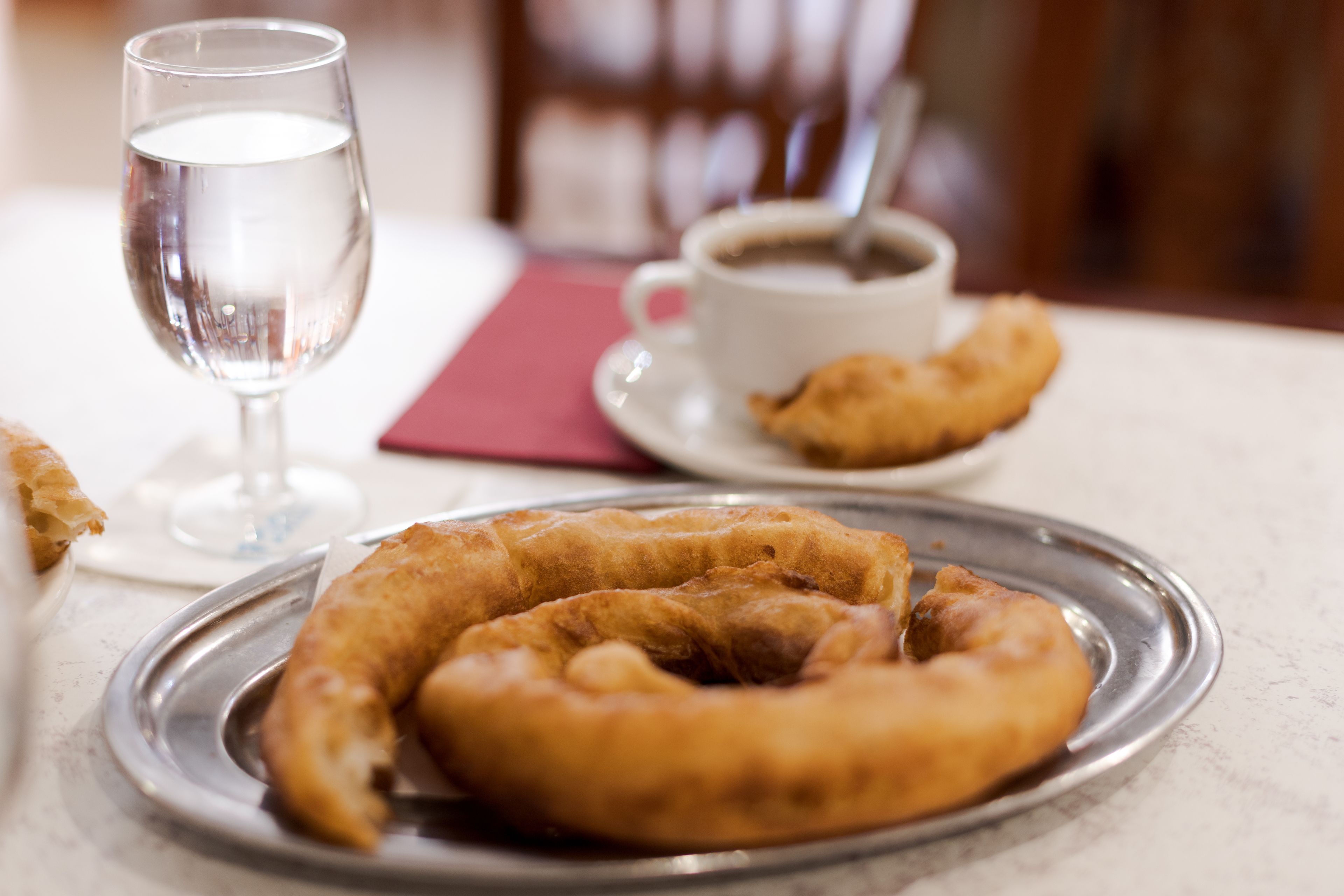 A plate of fried dough rings on a table with a glass of water and a cup of coffee.