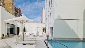 Un espace aménagé au bord de la piscine, avec des chaises longues et des parasols, une piscine, et un bâtiment au design moderne.