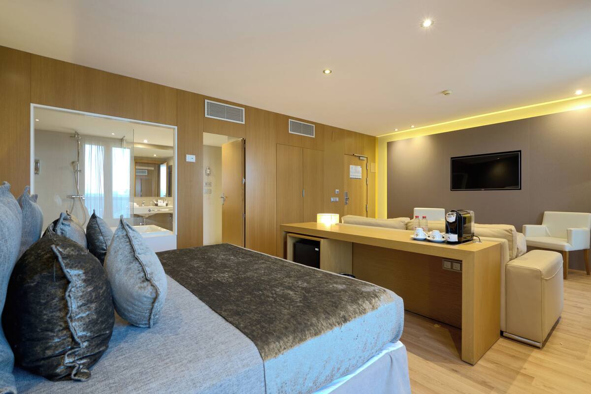 A modern hotel room with a bed, a desk, a TV, and a bathroom visible through an open door.