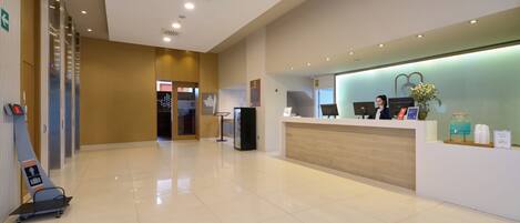 A modern hotel reception area with a clean, polished floor, a reception desk with computers, and a glass wall.