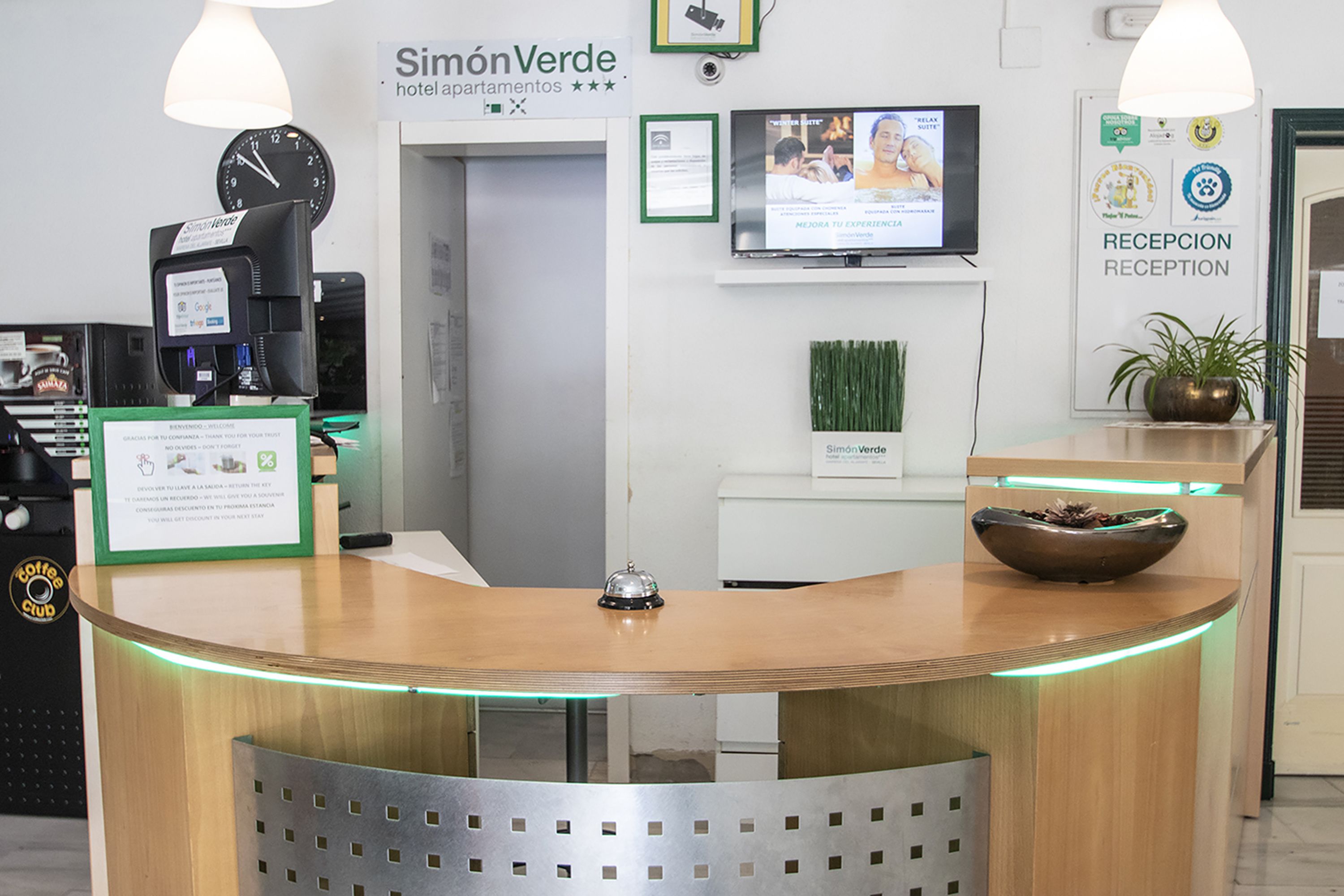 A reception desk with a clock, a television, and a sign for 'Simon Verde' hotel/apartments.