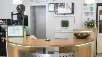 A reception desk with a clock, a television, and a sign for 'Simon Verde' hotel/apartments.
