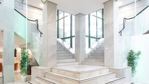 A modern interior with a central staircase, glass railings, and a marble floor.