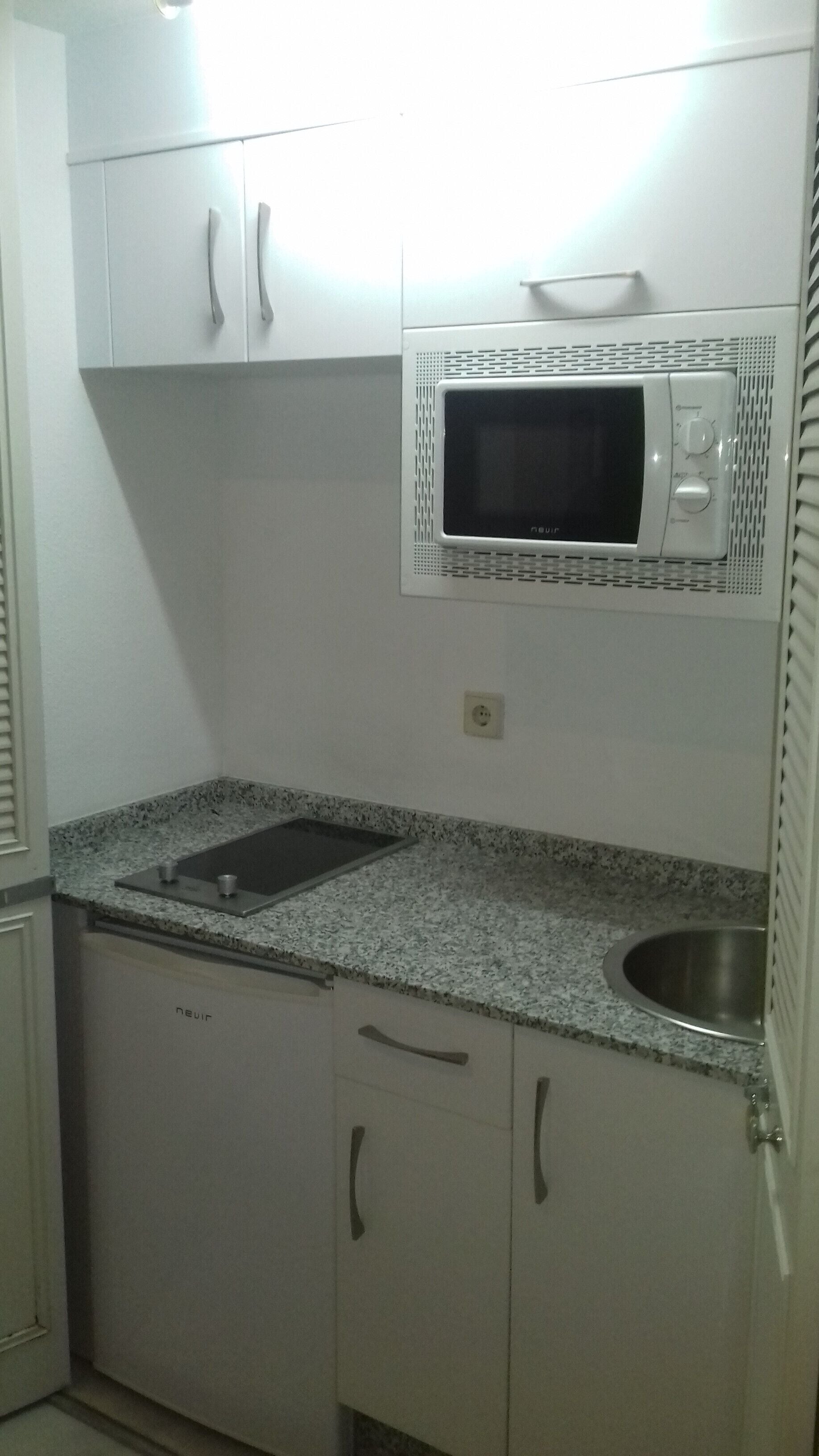 Een keuken met witte kastjes, een granieten aanrecht, een roestvrijstalen spoelbak en een magnetron.