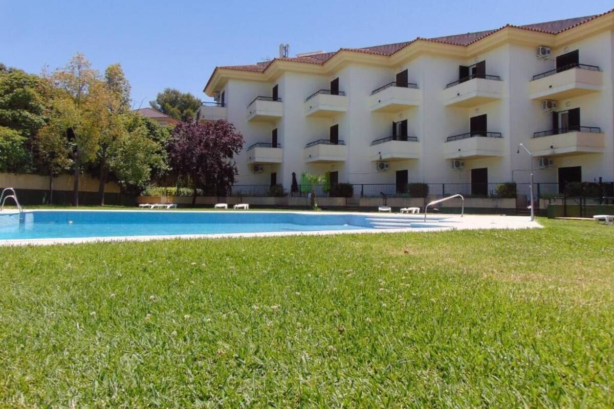 A hotel with a swimming pool, multiple balconies, and a well-maintained lawn.