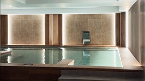 A modern indoor pool with a clear view of the water, a built-in water feature, and steps leading down to the pool.