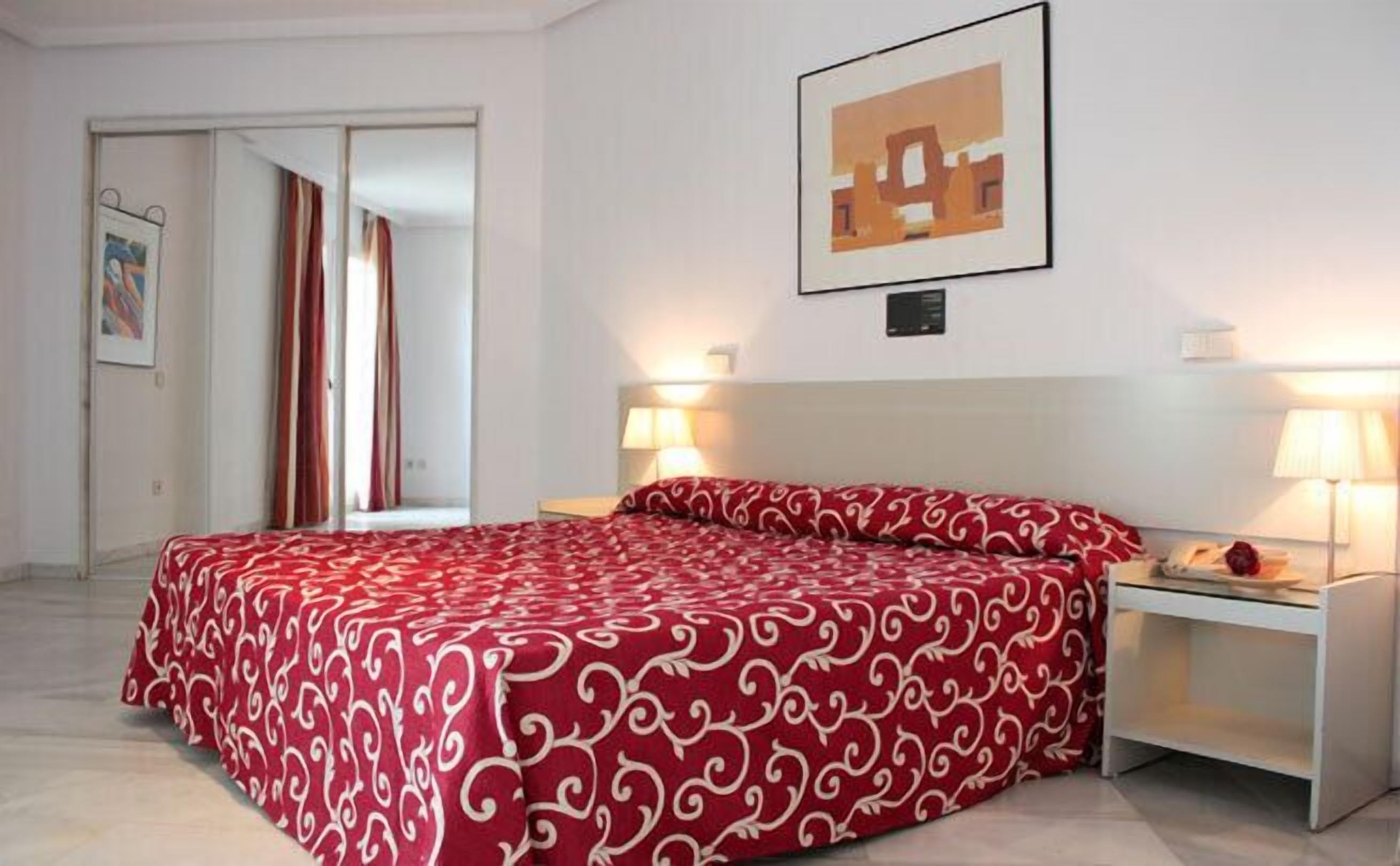 A hotel room with a bed, two bedside lamps, a nightstand, and a framed picture on the wall.