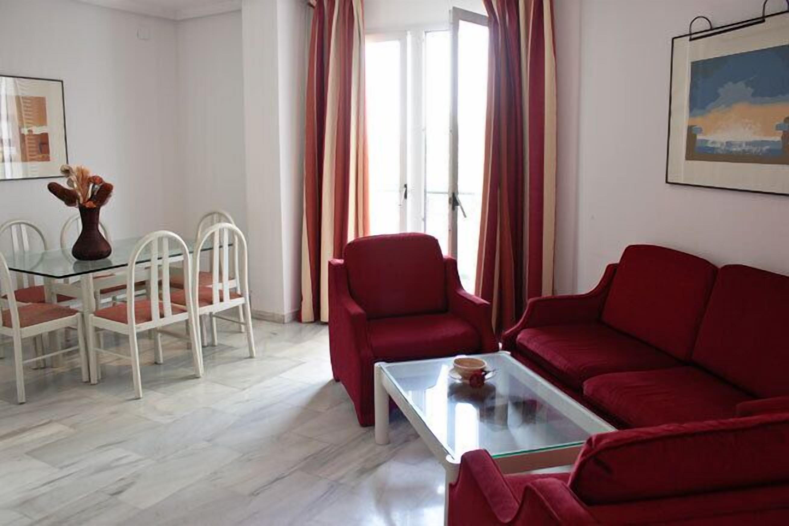 Un salón con una mesa de centro de vidrio, sofá rojo, sillas blancas y una mesa de comedor.