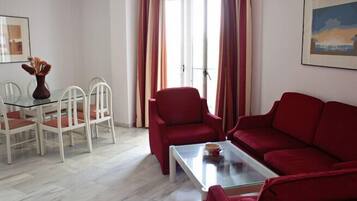 Un salón con una mesa de centro de vidrio, sofá rojo, sillas blancas y una mesa de comedor.