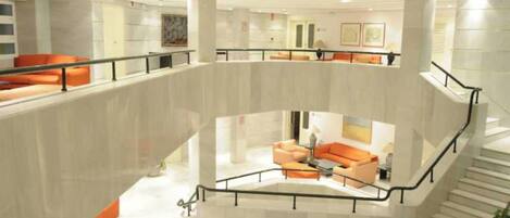 Un vestíbulo de varios niveles con una zona de estar central, una escalera y una barandilla de vidrio.