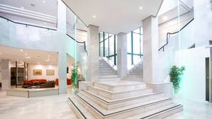 A spacious lobby with a marble staircase, modern furniture, and large windows.
