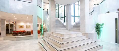 A spacious lobby with a marble staircase, modern furniture, and large windows.