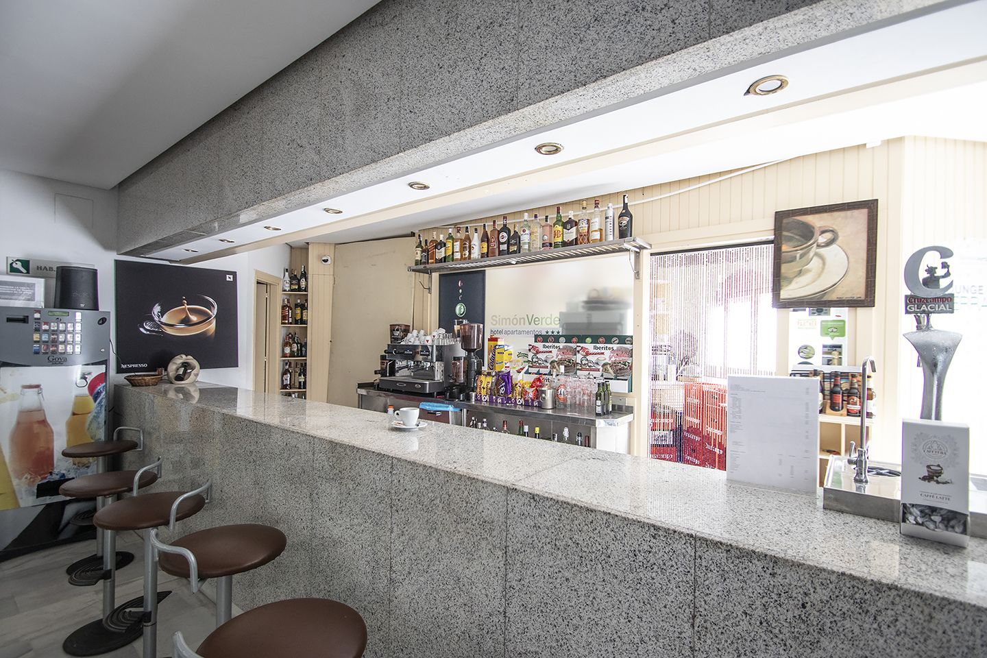 Zona de bar con mostrador, máquina de café espresso y asientos.