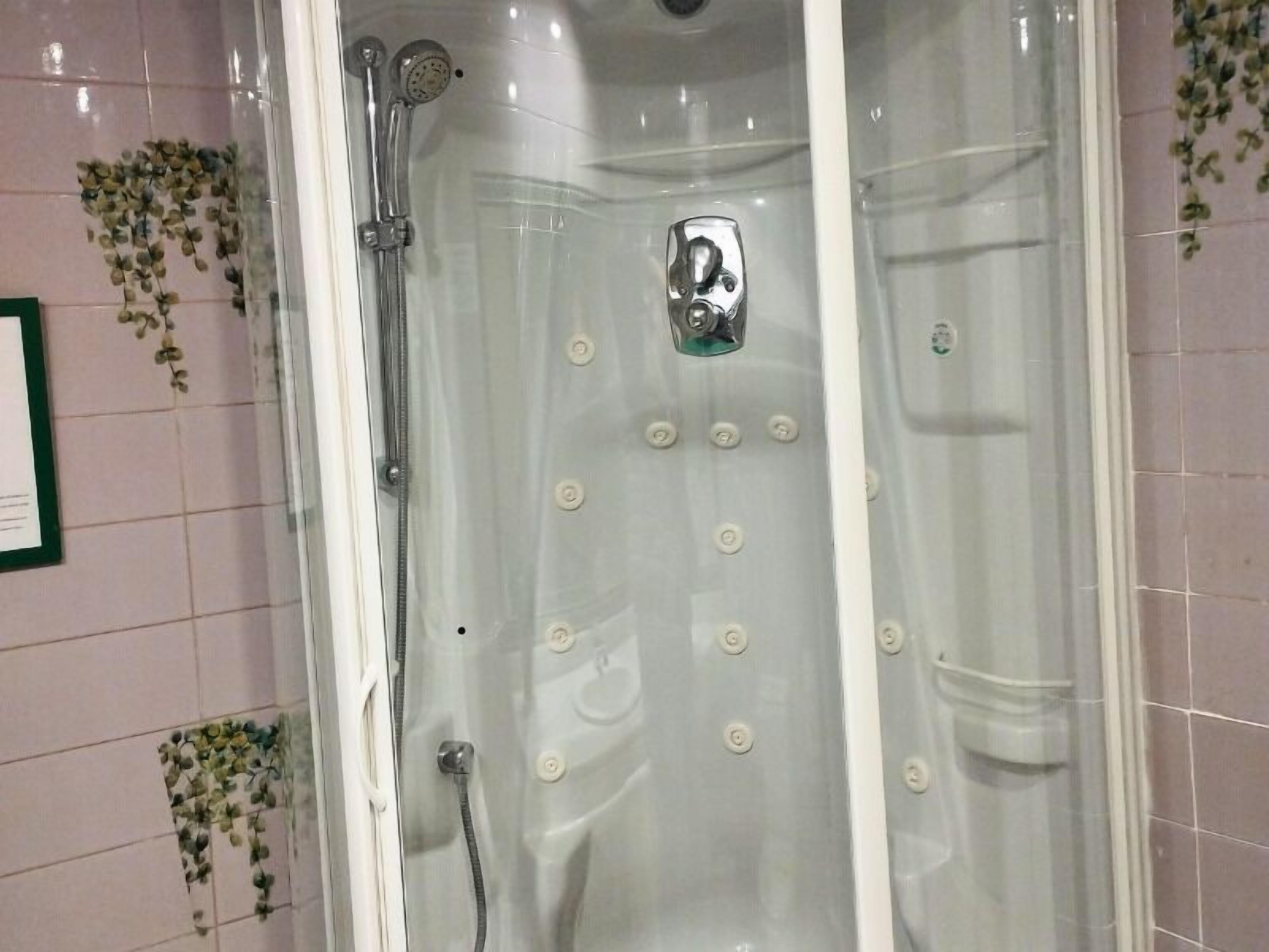 Cabina de ducha con paredes de vidrio, cabezal de ducha de mano y panel de control en la pared.