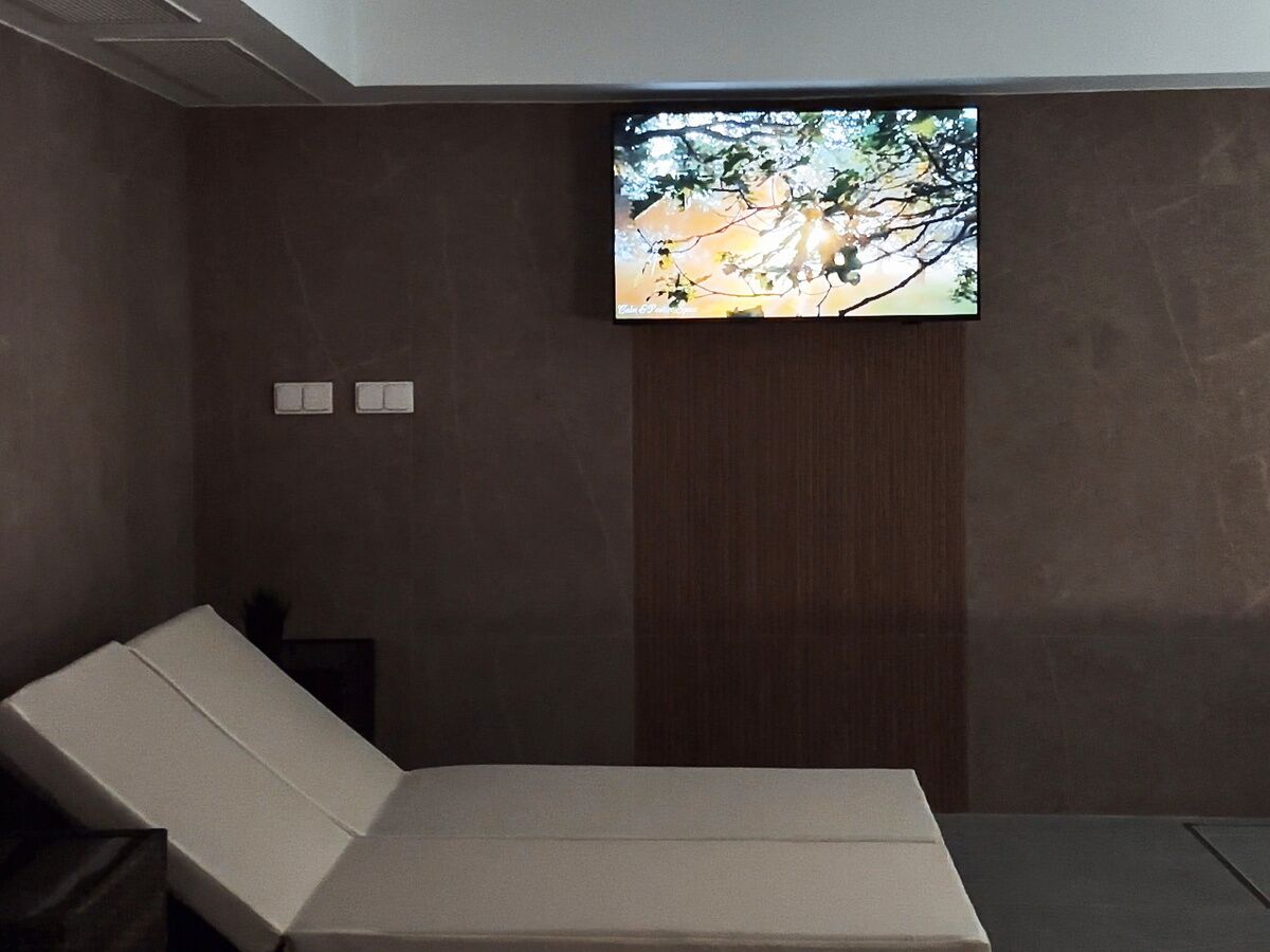 A modern room with a single bed, a flat-screen TV mounted on the wall, and a small table.