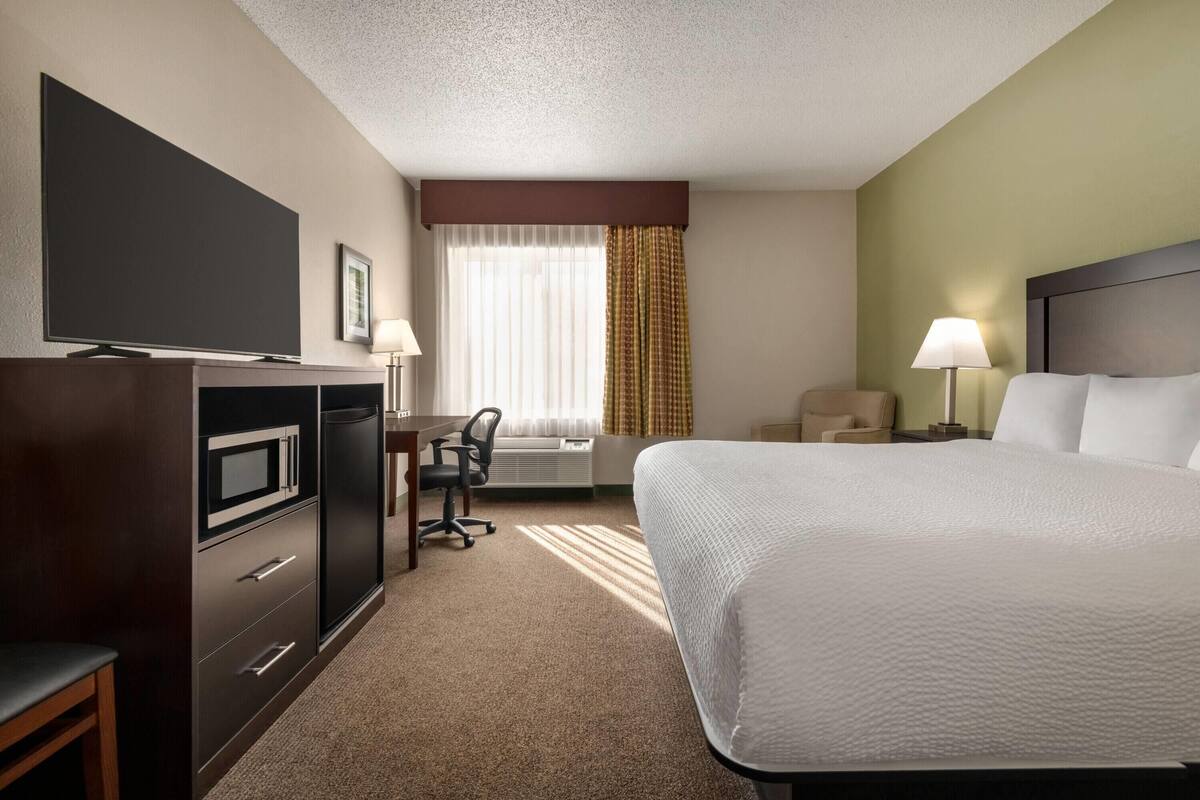 Una habitación de hotel con una cama, un escritorio con una silla, una televisión y una lámpara.