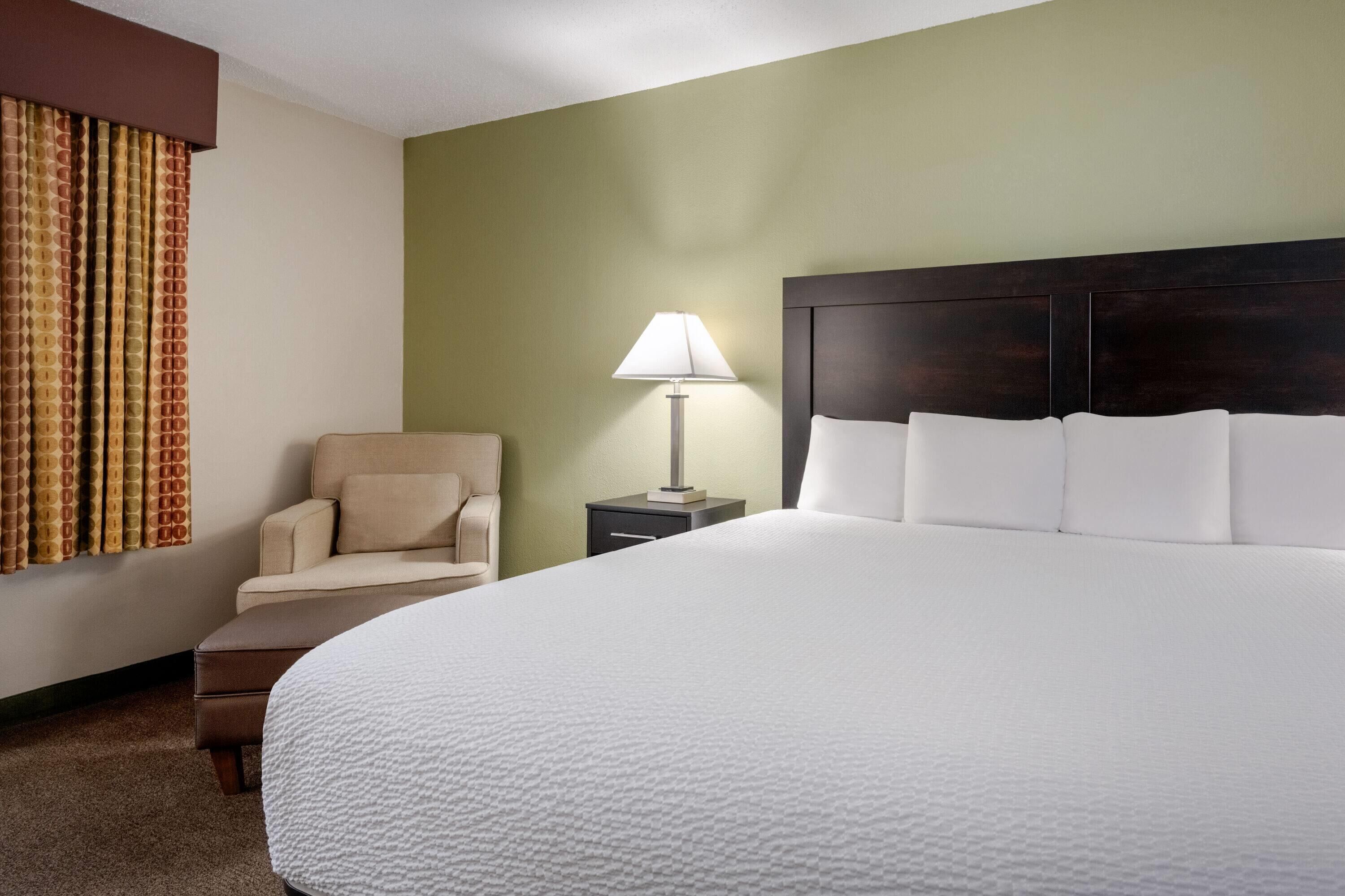 Una habitación de hotel con una cama grande, una silla, una mesita de noche y una lámpara.