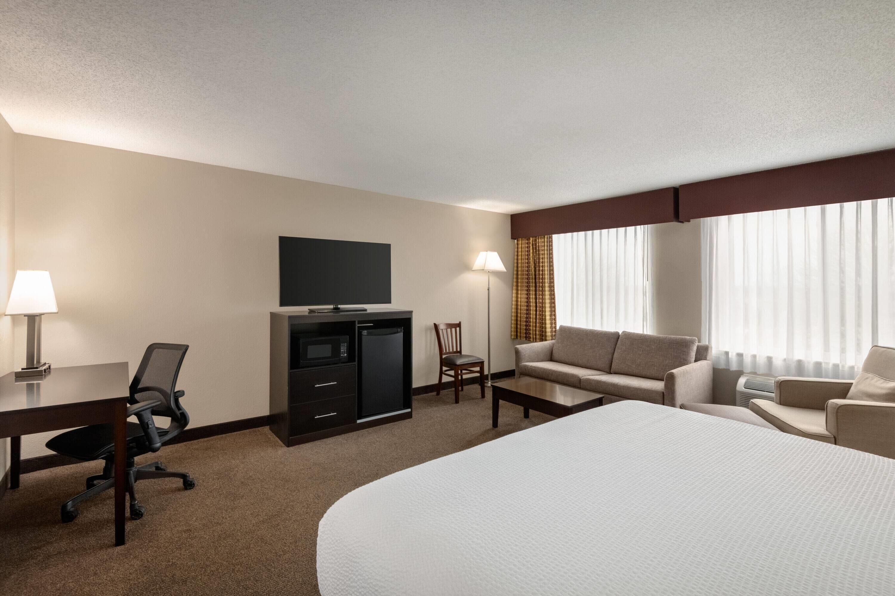 Ein Hotelzimmer mit einem Bett, einem Schreibtisch mit Lampe, einem Fernseher, einer Couch und einem Sessel.