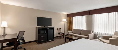 Ein Hotelzimmer mit einem Bett, einem Schreibtisch mit Lampe, einem Fernseher, einer Couch und einem Sessel.