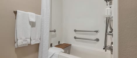 A bathroom with a bathtub, shower, and handrails.