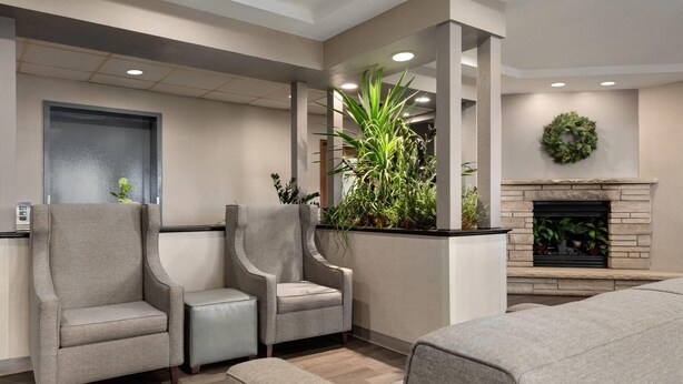 A modern lobby with two armchairs, a sofa, a fireplace, and a large potted plant. - Baymont by Wyndham Rockford (Rockford)