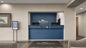 A reception desk with a blue backdrop, a framed picture on the wall, and a carpet with the hotel's name. - Baymont by Wyndham Rockford (Rockford)