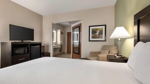A hotel room with a large bed, a television, a desk with a lamp, a chair, and a door leading to a bathroom. - Baymont by Wyndham Rockford (Rockford)