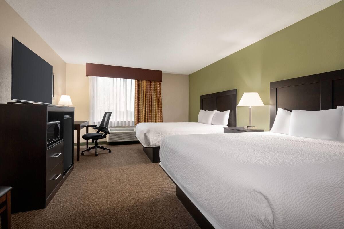 Habitación de hotel con dos camas, un escritorio, un televisor, una silla y una ventana con cortinas.