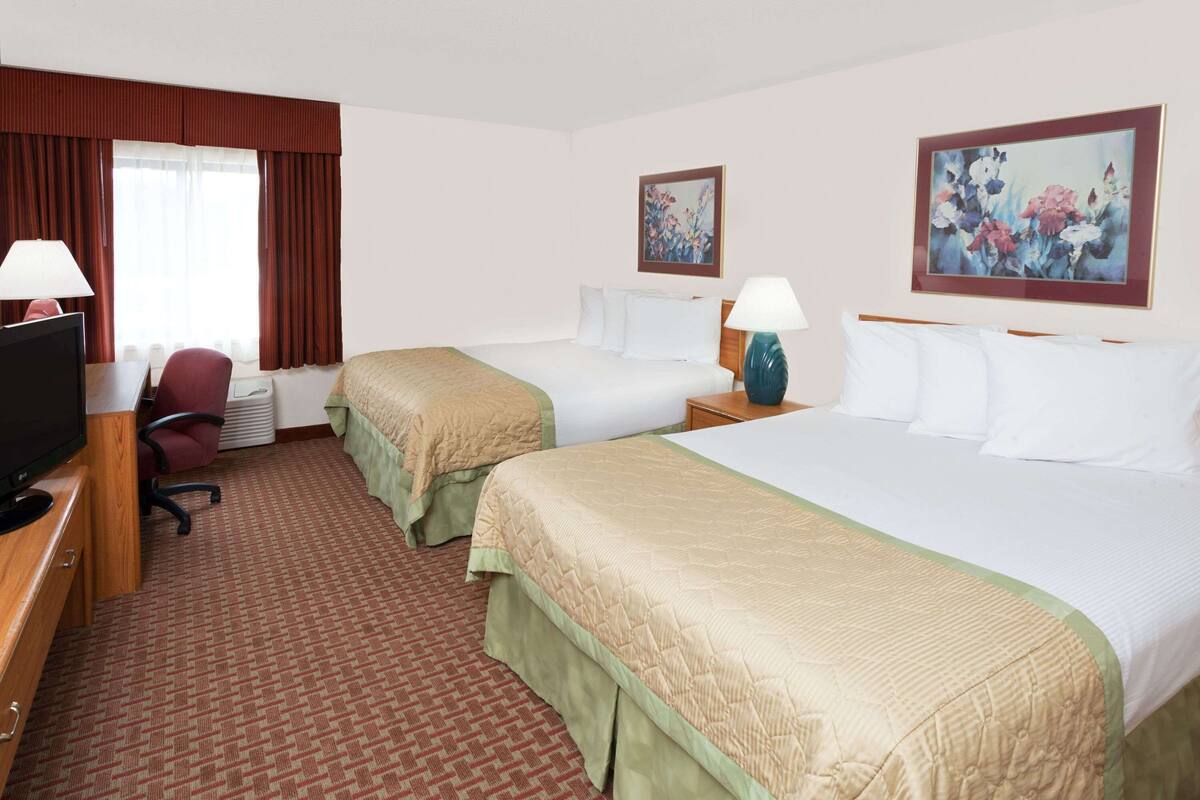 A hotel room with two beds, a desk with a television, a chair, and a window with curtains.
