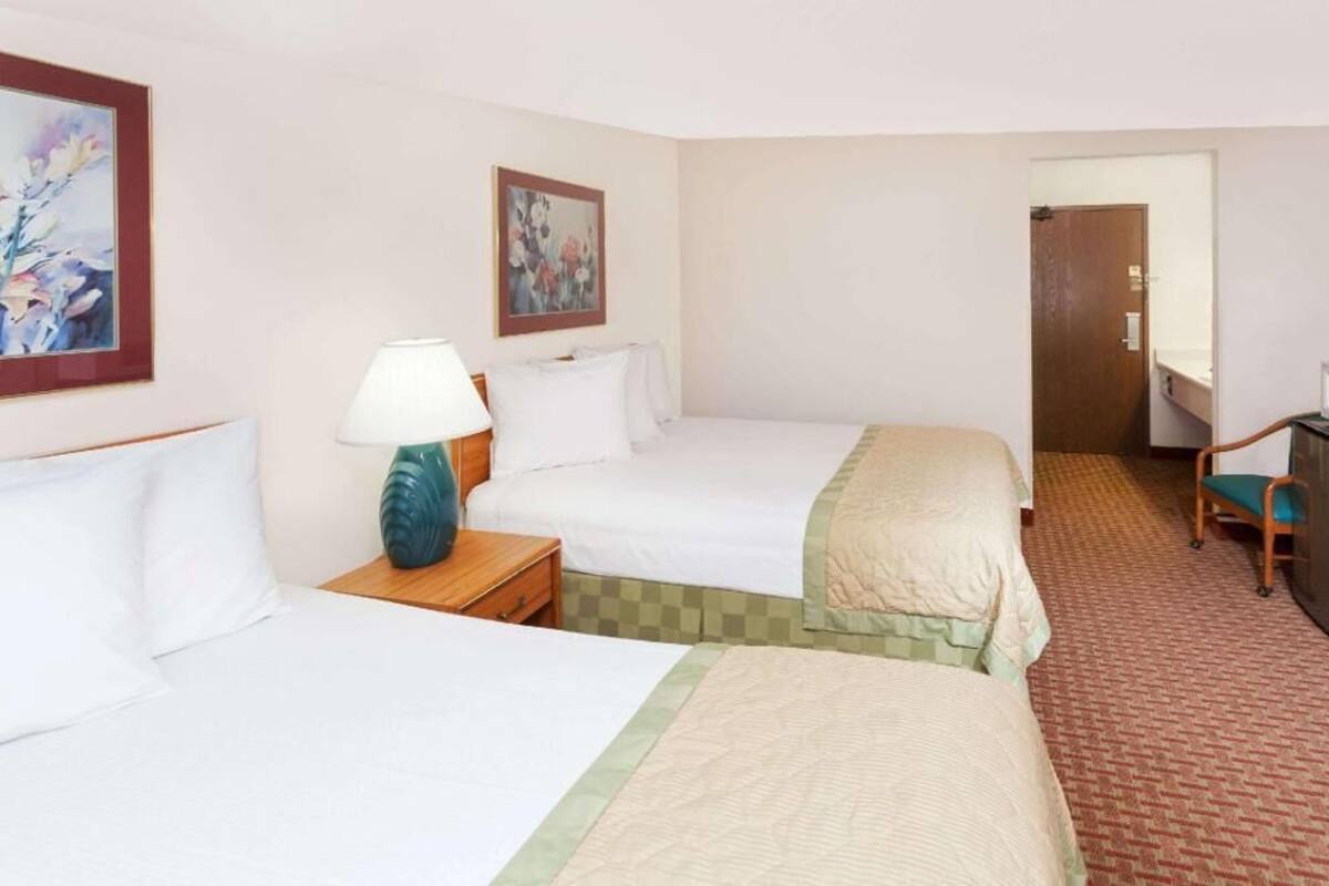 A hotel room with two beds, a desk, a chair, a lamp, and artwork on the walls.