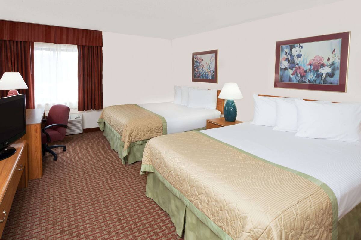 A hotel room with two beds, a desk with a television, a chair, and two lamps.