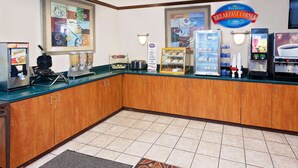 A breakfast corner with a coffee machine, a refrigerated display, and a sign reading "Breakfast Corner". - Baymont by Wyndham St. Joseph/Stevensville (Stevensville)
