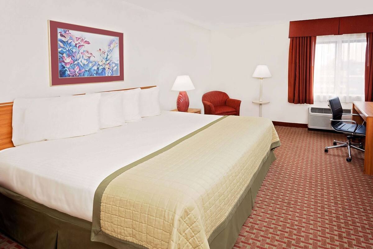 A hotel room with a large bed, two chairs, a desk, and a painting on the wall.
