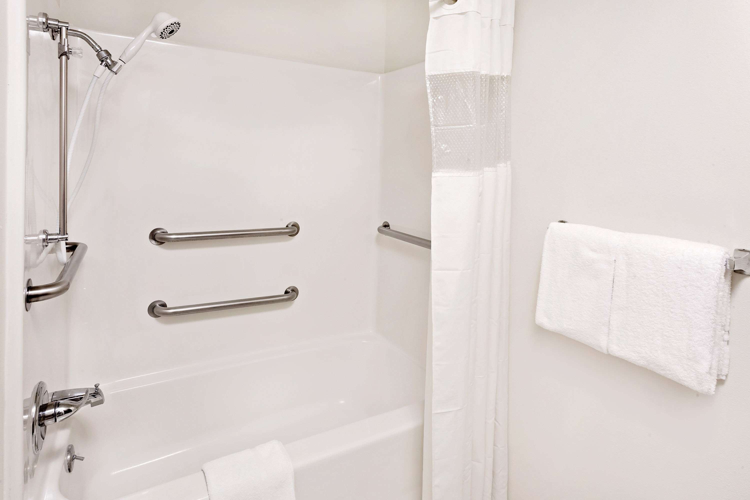 Un baño con bañera, barras de apoyo, cabezal de ducha y un perchero para toallas.