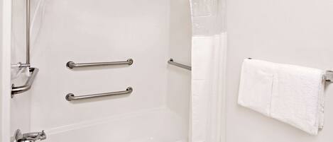 A bathroom with a bathtub, grab bars, a showerhead, and a towel rack.