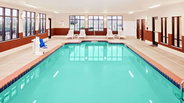 A swimming pool with multiple lounge chairs and a lifeguard chair, surrounded by windows and doors. - Baymont by Wyndham St. Joseph/Stevensville (Stevensville)