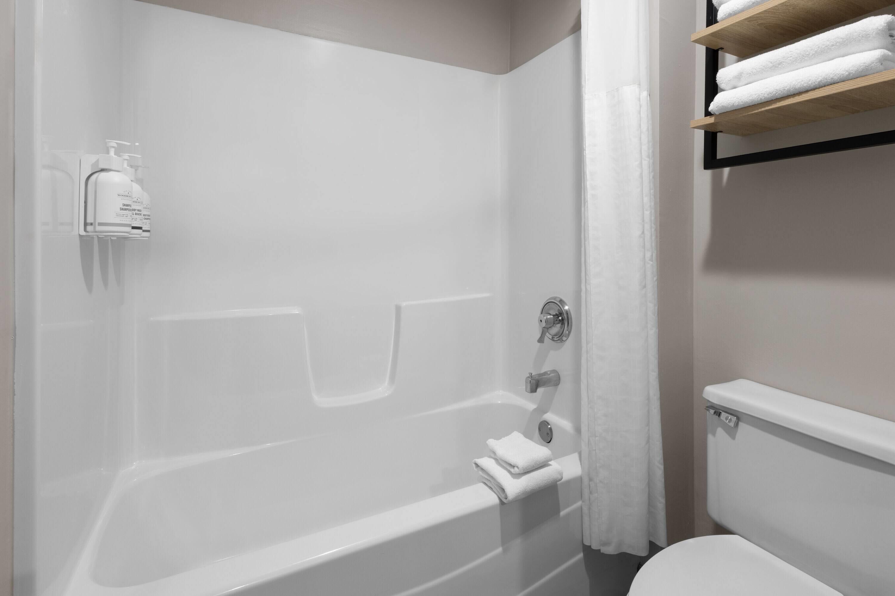 A bathroom with a bathtub, a toilet, and a shelf with towels.