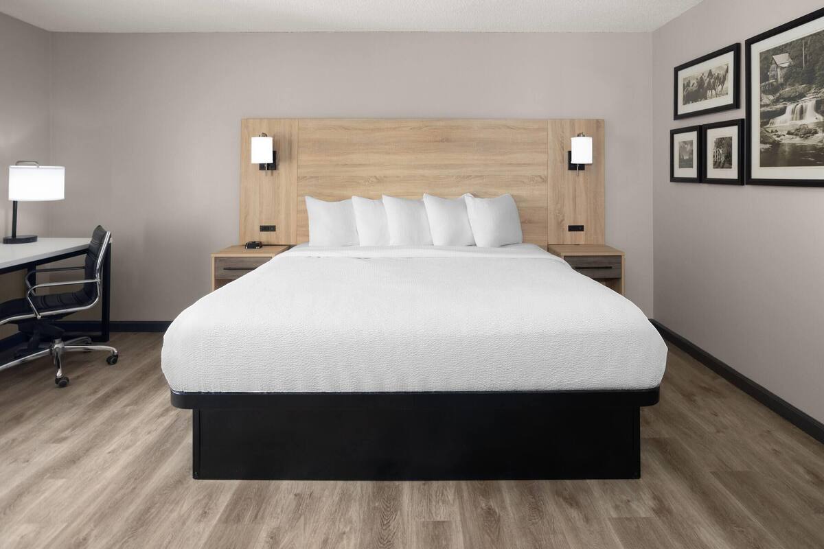 Ein Hotelzimmer mit einem großen Bett, Nachttischen mit Lampen, einem Schreibtisch mit Stuhl und gerahmten Bildern an der Wand.