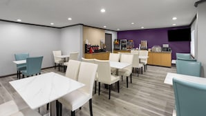 Un comedor moderno con sillas blancas y azul turquesa, mesas de mármol y una cocina al fondo.