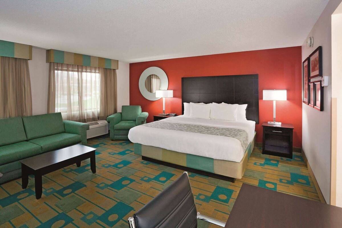 Ein Hotelzimmer mit Bett, grünem Sofa, einem kleinen Tisch, einem Sessel und einem Schreibtisch.