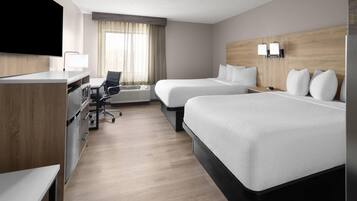 A hotel room with two beds, a desk, a chair, a TV, and a window with curtains.