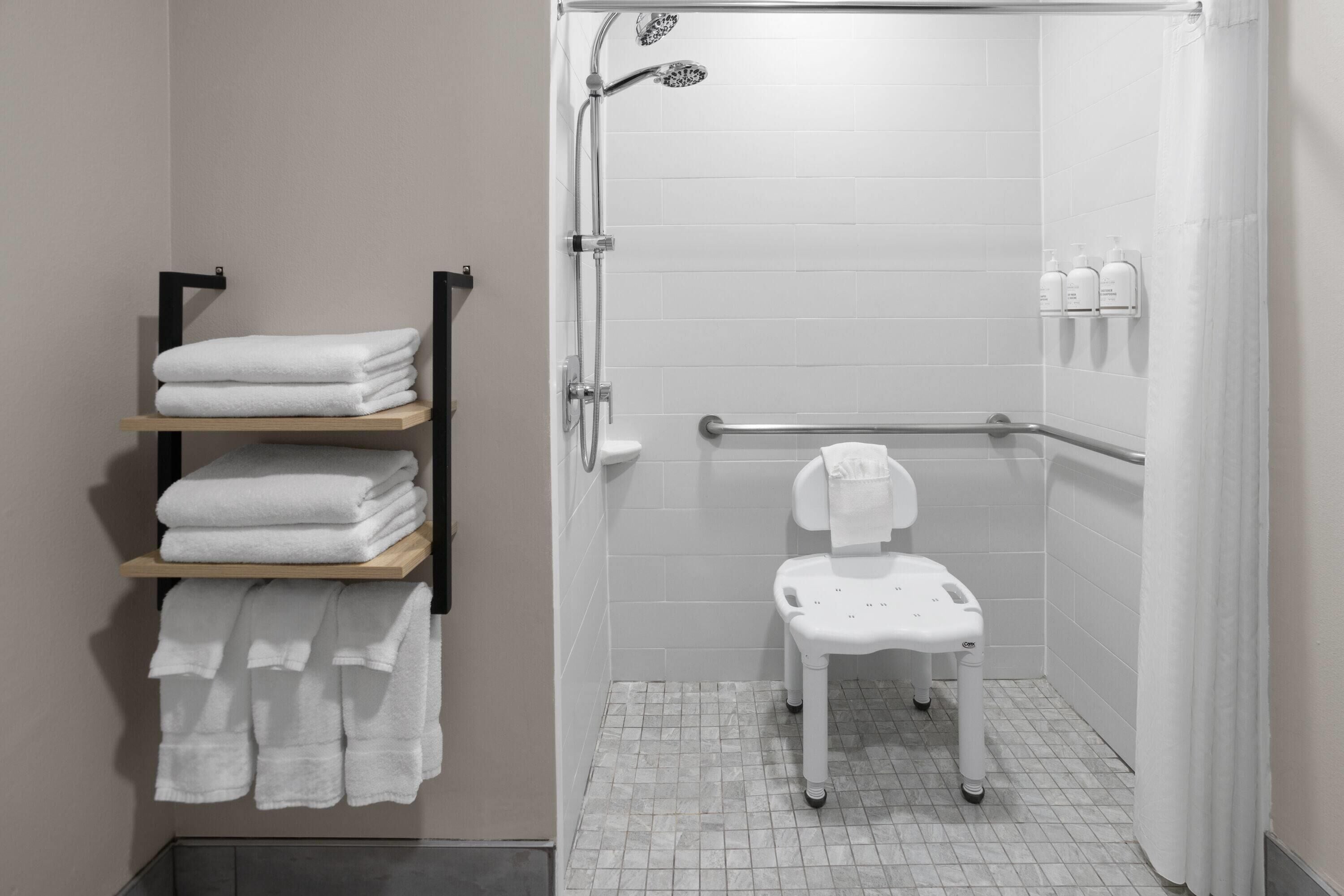 Un área de ducha moderna con un inodoro blanco, un perchero con toallas dobladas y un dispensador de gel hidroalcohólico.